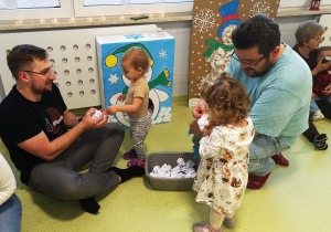 Dziewczynki z rodzicami bawią się w celowanie kulkami do bałwanka.