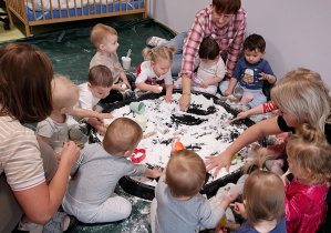 Dzieci z pomocą opiekunek bawią się sensorycznie sztucznym śniegiem.