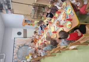 Dzieci siedzą przy stolikach podczas urodzinowego poczęstunku.