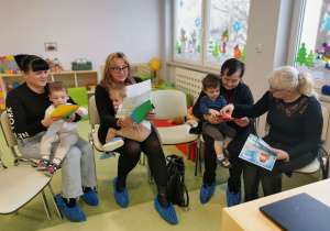 Wnuczki z babciami siedzą i oglądają prezentację z okazji Dnia Babci i Dziadka.