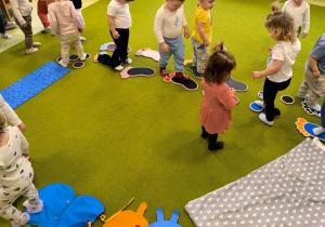 Dzieci chodzą po podłodze na której rozłożone są akcesoria sensoryczne które tworzą ścieżkę.