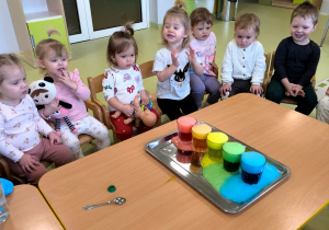 Dzieci siedzą przy stole i oglądają doświadczenie chemiczne.