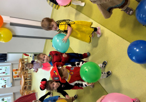 Dzieci tańczą na dywanie z kolorowymi balonami.