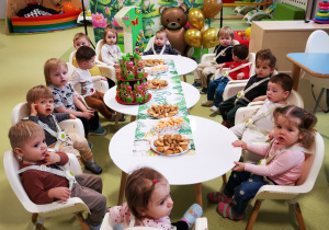 Leoś z dziećmi siedzi przy stole podczas urodzinowego poczęstunku.