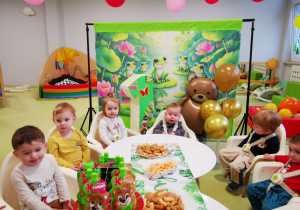 Leoś z dziećmi siedzi przy stole podczas urodzinowego poczęstunku.