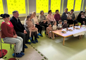 Babcie i Dziadkowie siedzą przy stole i oglądają prezentację.