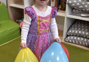 Rozalka pozuje do zdjęcia. W rączkach trzyma żółty i niebieski balonik.