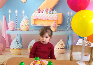 Małgosia siedzi przy stole i je urodzinowy poczęstunek.