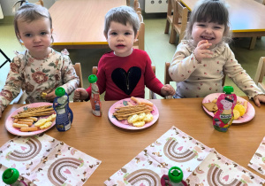 Dzieci siedzą przy stole i jedzą urodzinowy poczęstunek.