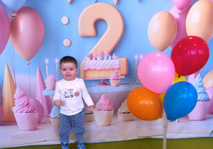 Dawidek pozuje do urodzinowego zdjęcja z kolorowymi balonami.