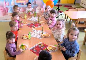 Dawidek i dzieci siedzą przy stole i jedzą urodzinowy poczęstunek.