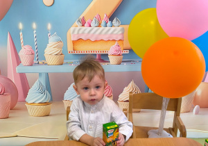 Staś siedzi przy stole je urodzinowy poczęstunek .