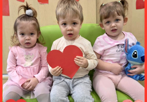 Marcelina, Franek i Tola siedzą na zielonej kanapie i pozują do zdjęcia z czerwonymi serduszkami z okazji Walentynek.