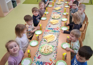Dzieci siedzą przy stole na którym znajduje się urodziny poczestunek.