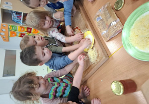 Dzieci rozkładają składniki na pizzy.