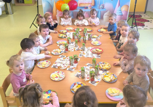 Wszystkie dzieci siedzą przy stole i jedzą urodzinowy poczęstunek.