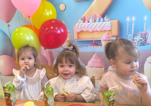 Dzieci siedzą przy stole i jedzą urodzinowy poczęstunek.