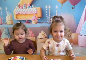 Rozalia i Amelia siedzą przy stole i jedzą urodzinowy poczęstunek.