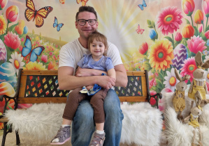 Aniela wraz z tatą siedzi na ławeczce i pozują na Wielkanocnym tle.