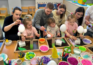 Antonina, Tola i Rozalia razem z rodzicami dekorują świąteczne ozdoby Wielkanocne hiacynta i jajka styropianowe.