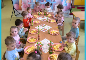 Dzieci siedzą przy stole i jedzą urodzinowy poczęstunek.
