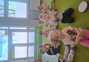 Dzieci grają na instrumentach muzycznych siedząc na dywanie.