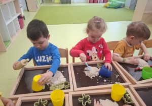 Leon, Hania i Stanisław bawią się przy stoliku piaskiem kinetycznym.