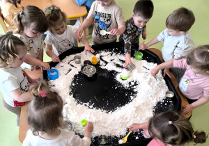 Dzieci siedzą przy stoliku i bawią się piaskiem kinetycznym.