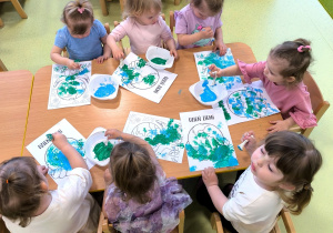 Dzieci siedzą przy stolikach i wykonują pracę plastyczną z okazji Dnia Ziemi. Malują farbami kulę ziemską.