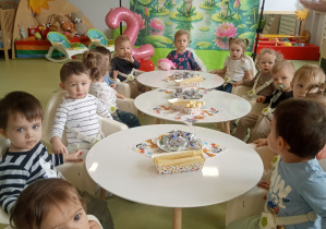 Tosia siedzi przy urodzinowym stole z dziećmi.