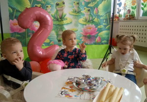 Tosia z dziećmi siedzi przy stole, częstuje się smakołykami urodzinowymi.