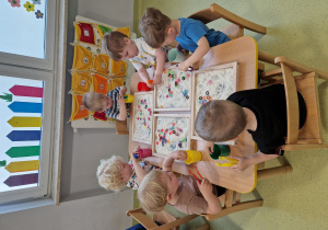 Dzieci siedzą przy stoliku i pęsetką wyciągają gumki z ryżu.