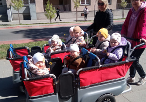 Dzieci z opiekunkami są na spacerze w wózku wieloosobowym.
