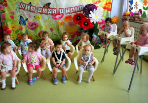Dzieci siedzą na krzesełkach i czekają na rodziców z okazji uroczystości Dnia Mamy i Taty.