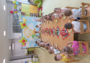 Dzieci siedzą przy stole i jedzą urodzinowy poczęstunek.