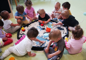 Dzieci bawią się piaskiem kinetycznym na dużej tacy sensorycznej.