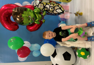 Antoś siedzi na krześle i pozuje do zdjęcia z balonami.
