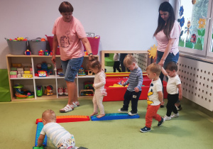 Dzieci z pomocą opiekunek przechodzą po sensorycznym torze ćwicząc równowagę.