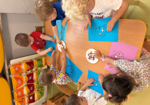 Dzieci siedzą przy stole i wyklejają ryby z plasteliny.