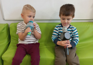 Czarek i Szymon siedzą na zielonej kanapie trzymają mikrofony .