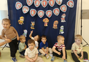 Chłopcy siedzą i pozują do zdjęcia grupowego na tle z okazji Dnia Chłopca.