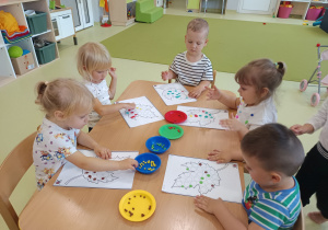 Dzieci siedzą przy stoliku i wyklejają jesiennego liścia plasteliną.