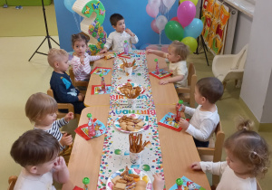 Dzieci siedzą przy stole jedzą urodzinowy poczęstunek.