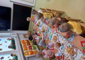 Dzieci siedzą przy stole i jedzą urodzinowy poczęstunek.